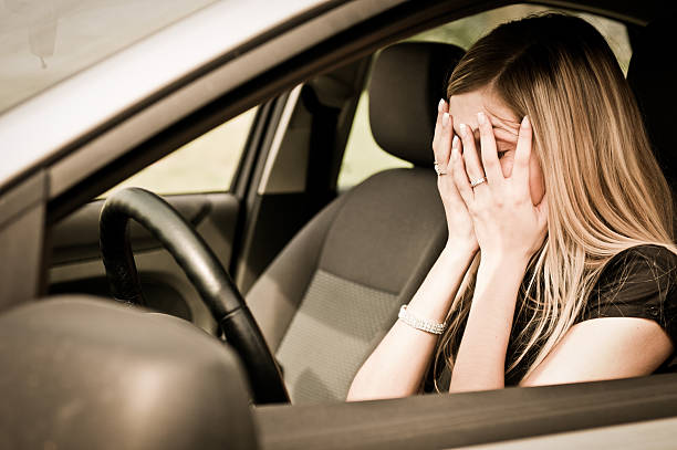 young woman with hands on eyes sitting depressed in car